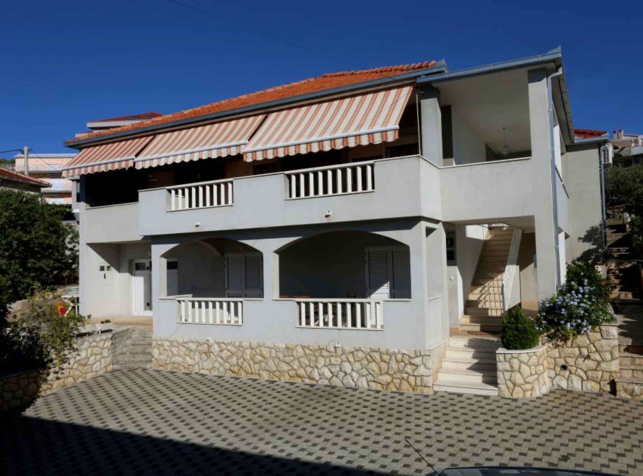 A two-story house with a stone foundation, a tiled roof, and a balcony with white railings.