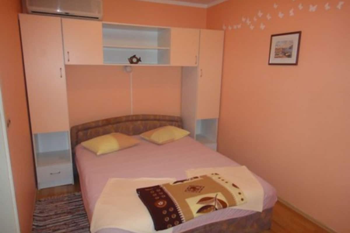 A bedroom with a bed, a wardrobe, a shelf, and a picture on the wall.