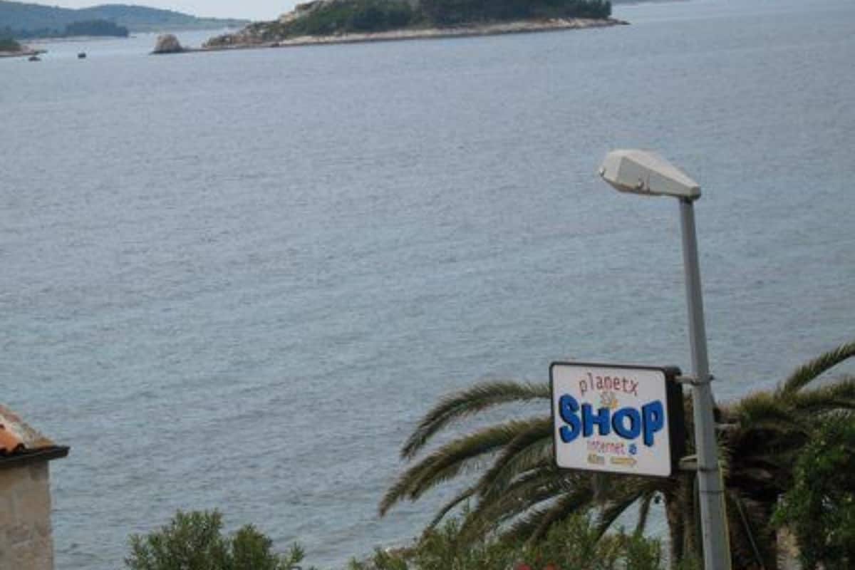 A sign for 'planetx SHOP' near a body of water with boats and a distant island.