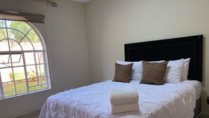 Een net opgemaakt bed met witte lakens en een opgevouwen handdoek, een zwart hoofdbord en twee kussens met luipaardprint.