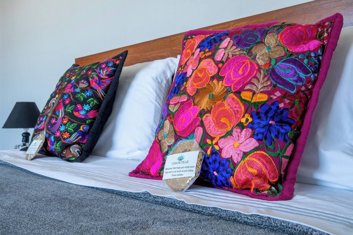 A bed with two colorful pillows, a wooden headboard, and a bedside table with a lamp.