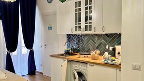 Cocina compacta con lavadora, encimera de madera y cama con manta color turquesa.