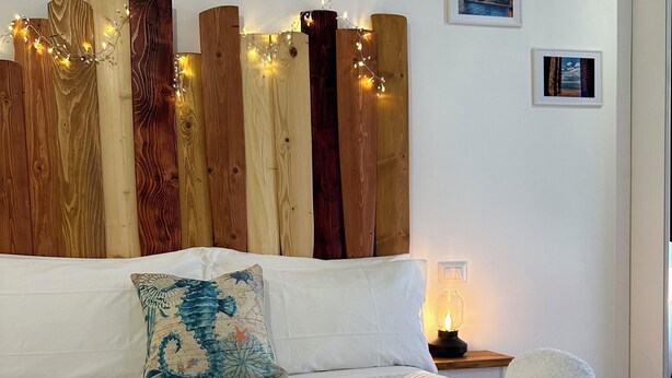 Un dormitorio con cabecera de madera, ropa de cama blanca y decoración temática náutica que incluye un ancla de cuerda y toallas.