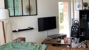 A living room with a sofa, a TV, a coffee table, and a bookshelf. - Granville, 50m from the sea, on the garden level, nice and cosy apartment-terrace for 2 persons (Granville)