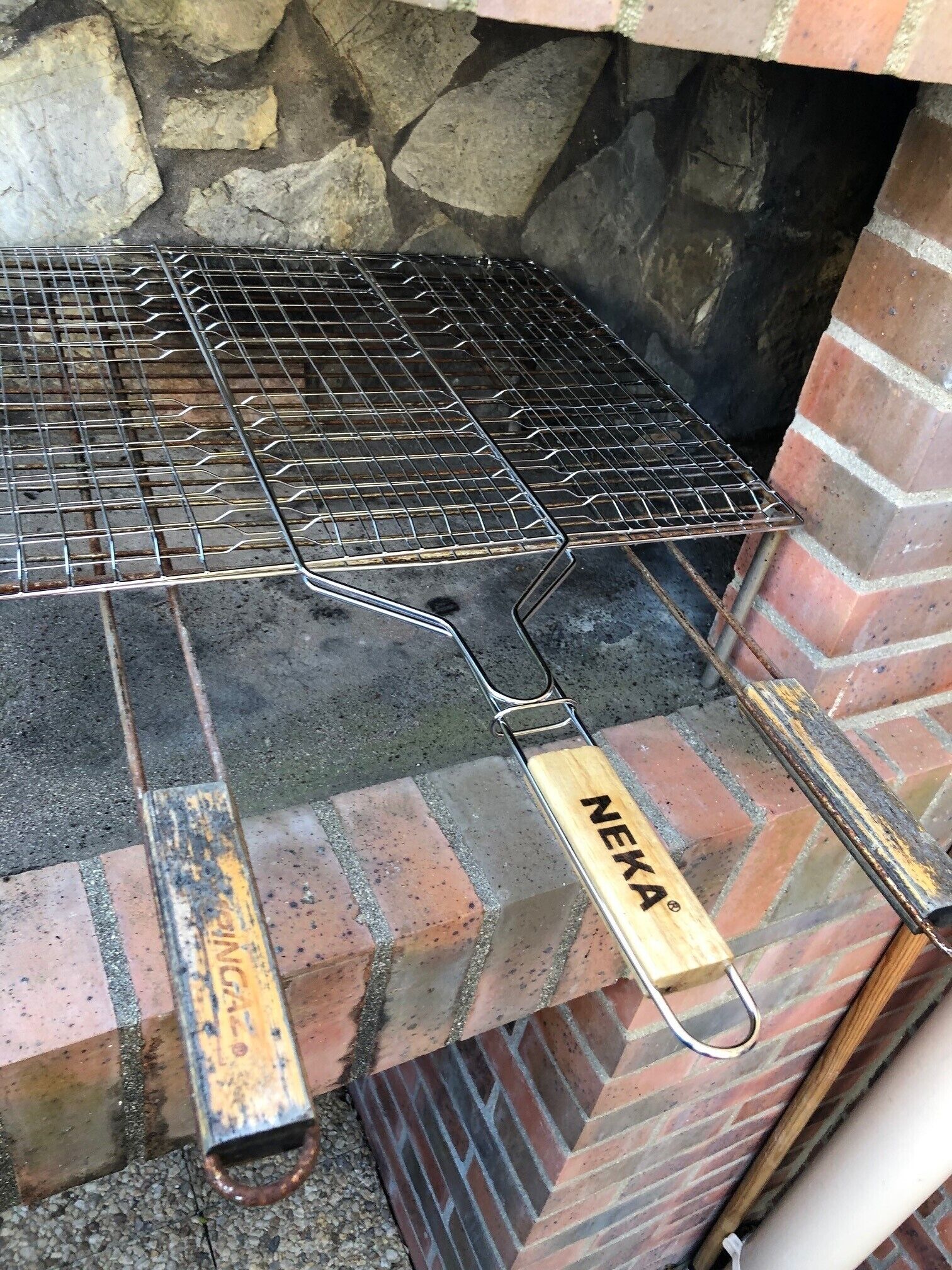 A metal grill grate with a metal handle, placed on a brick surface.