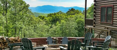 A wooden cabin with a deck, outdoor seating area with Adirondack chairs, and a scenic mountain view.
