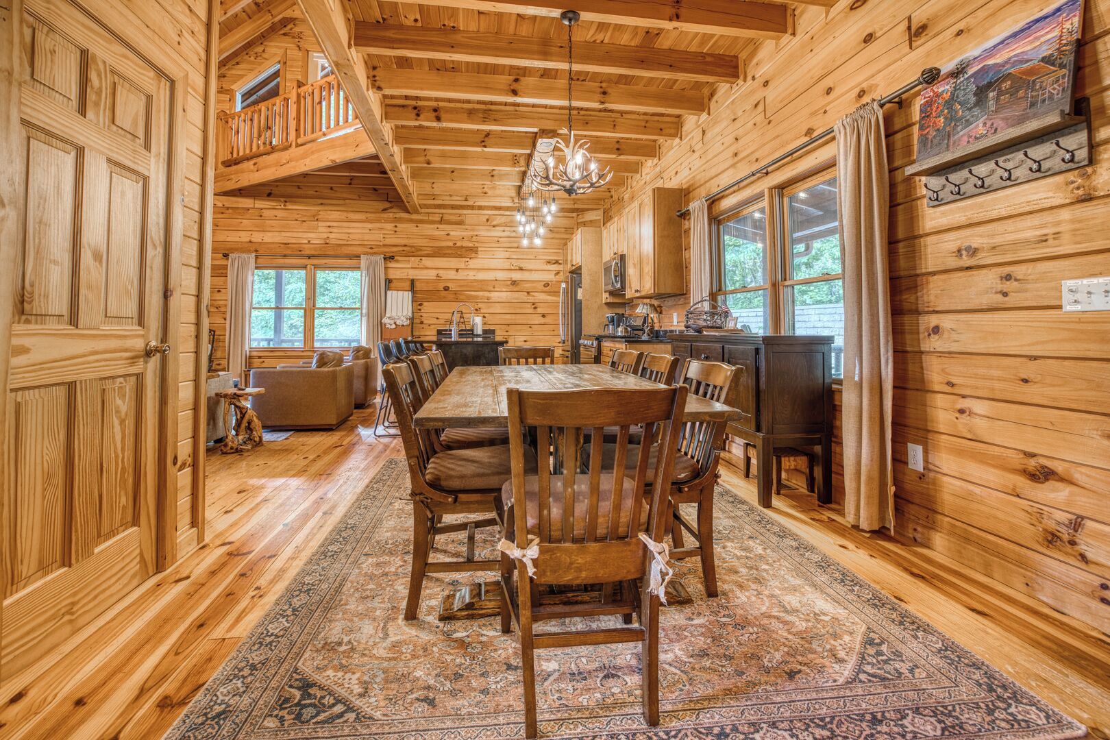 A wooden cabin interior with a dining area, kitchen, and large windows.