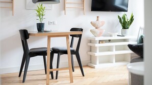 Un salon moderne avec une table à manger en bois, des chaises noires, un lampadaire noir, un téléviseur à écran plat fixé au mur et une étagère blanche.