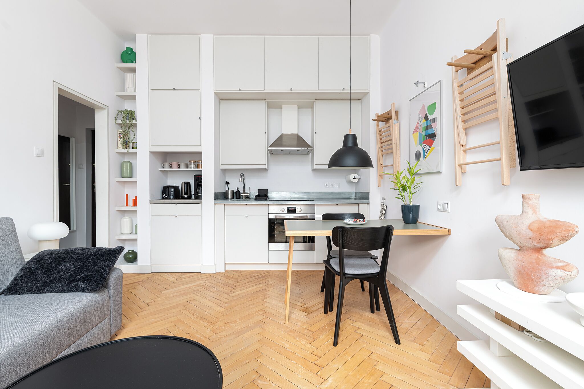 Une cuisine moderne avec des meubles blancs, un coin repas comprenant une table et des chaises, et un téléviseur fixé au mur.