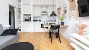 Une cuisine moderne avec des meubles blancs, un coin repas comprenant une table et des chaises, et un téléviseur fixé au mur.