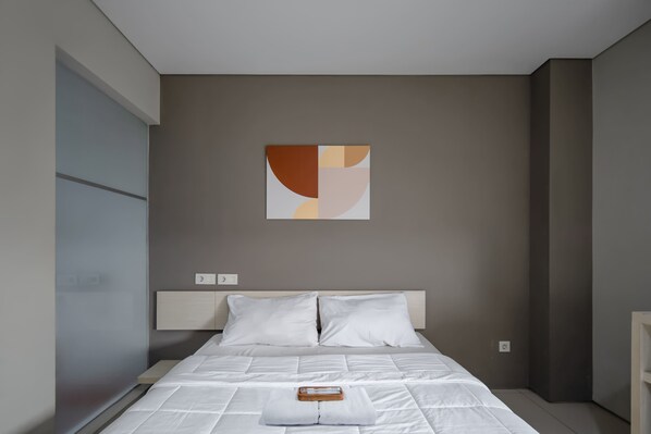 Quarto moderno com cama, roupa de cama branca, cabeceira e uma obra de arte abstrata pendurada na parede.
