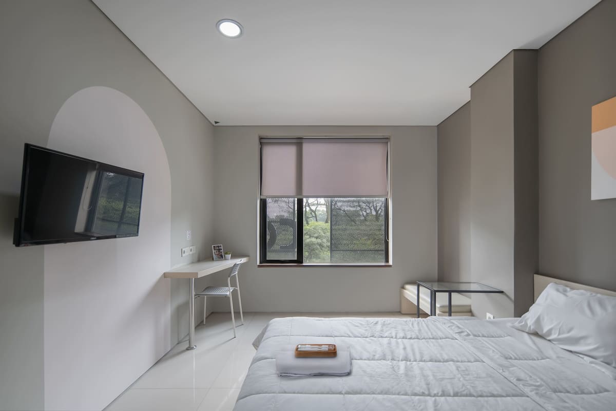 Ein modernes Schlafzimmer mit einem Bett, einem Schreibtisch und einem an der Wand befestigten Fernseher.
