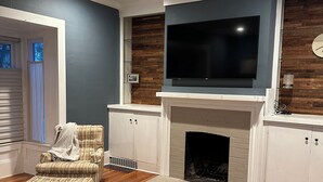 A modern living room with a fireplace, a television mounted above it, and a striped armchair. - Whole house - Park Ave 3 bedroom, enjoy all the neighborhood has to offer! (Rochester)