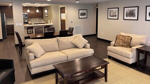 A modern living room with a sofa, coffee table, and a dining area with chairs and a kitchen in the background. - Beautiful Downtown Condo! Steps away from the best dining in town! (Tallahassee)