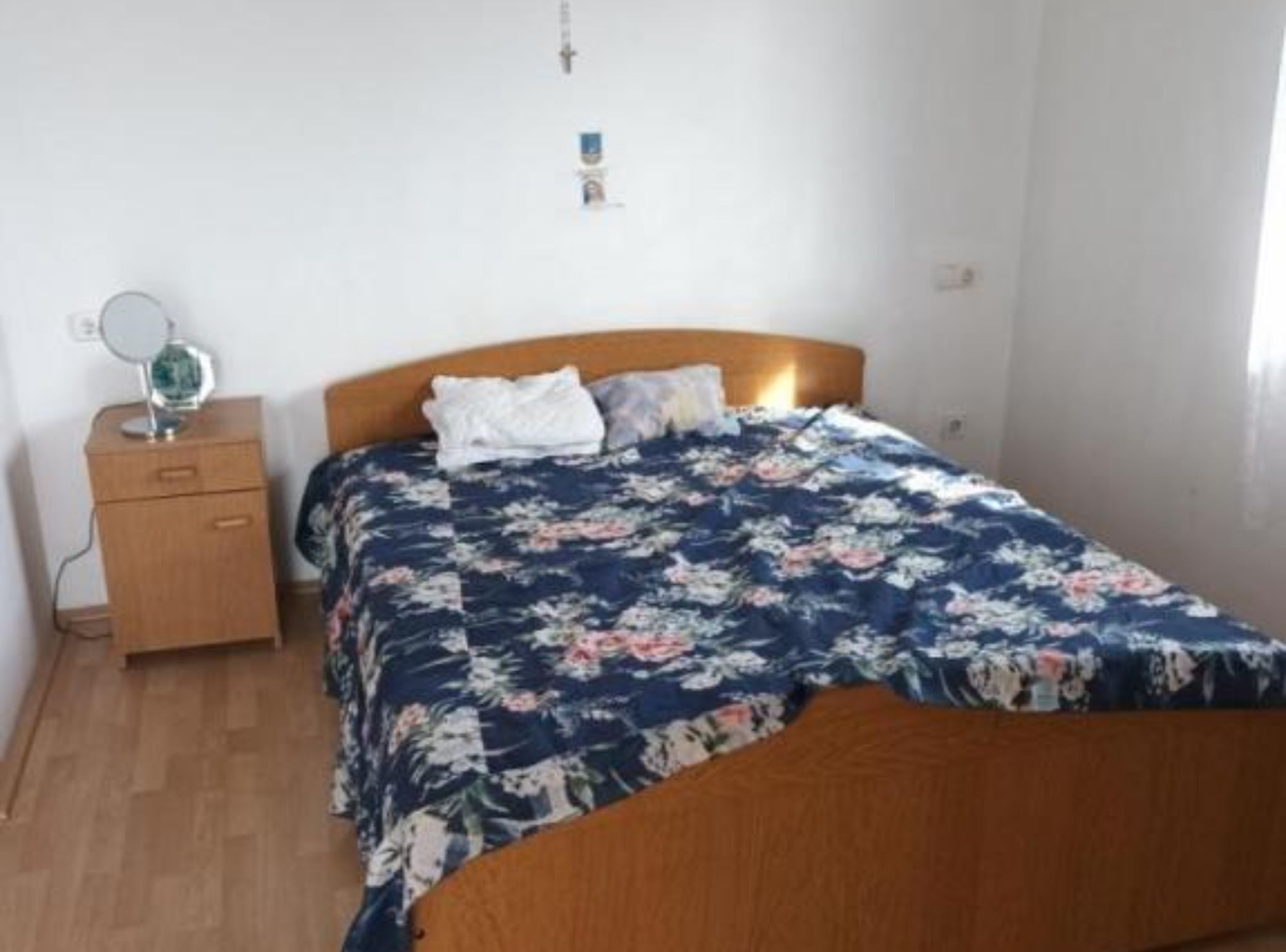 Une chambre à coucher avec un lit en bois, une table de chevet avec un miroir et une couvre-lit à motifs floraux.