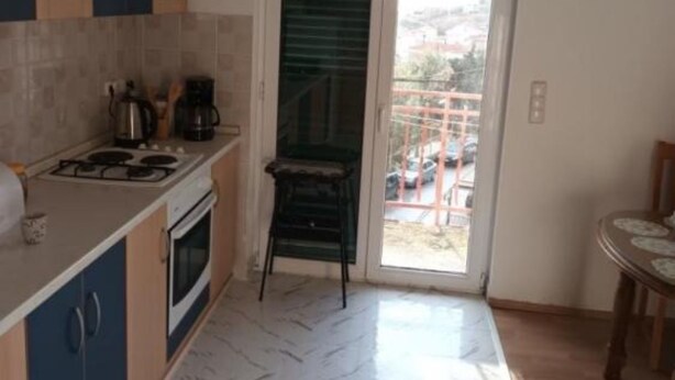 A compact kitchen with a gas stove, oven, and a coffee maker. A chair is placed near a sliding glass door leading to a balcony with a view of parked cars and buildings. - Spacious and Cozy Apartments Dugi Rat (Dugi Rat)