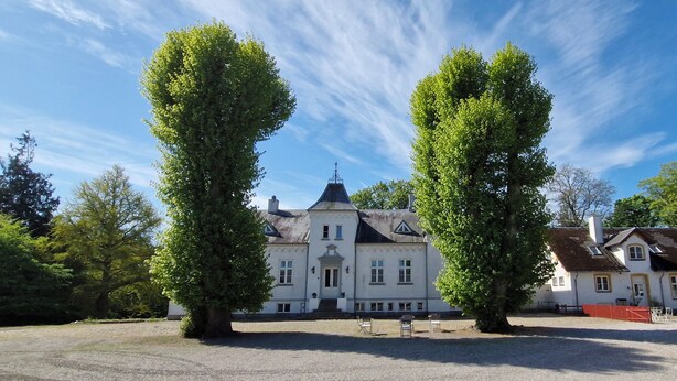 A large, historic building with symmetrical architecture, a central entrance, and a well-maintained lawn.