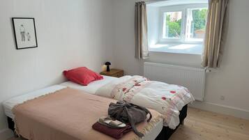 A bedroom with a bed, a bedside table with a lamp, a window with curtains, and a radiator.