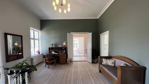 A room with a desk, chair, and a sofa. There is a mirror on the wall and a door leading to another room.