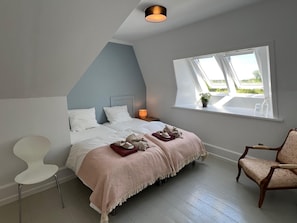 A bedroom with a bed, bedside table, chair, and a window with a view.