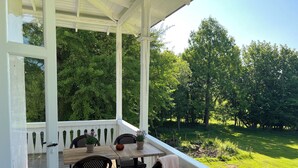 A covered porch with a wooden table and chairs, surrounded by a white railing.