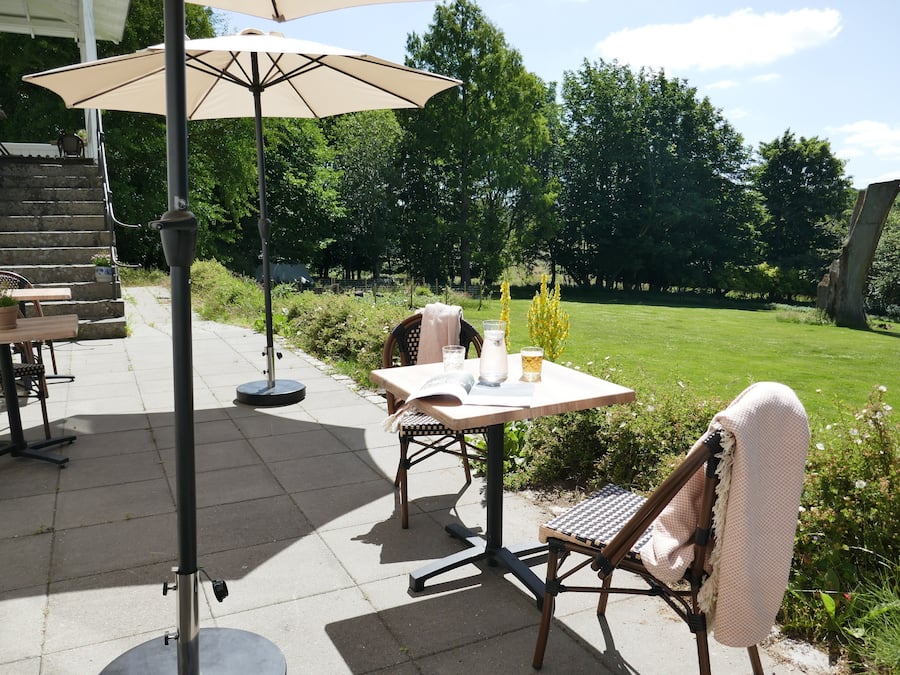 En udendørs patio med et bord, stole, en lampe og en stor parasol.