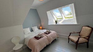 A bedroom with a bed, a chair, a window, and a nightstand.