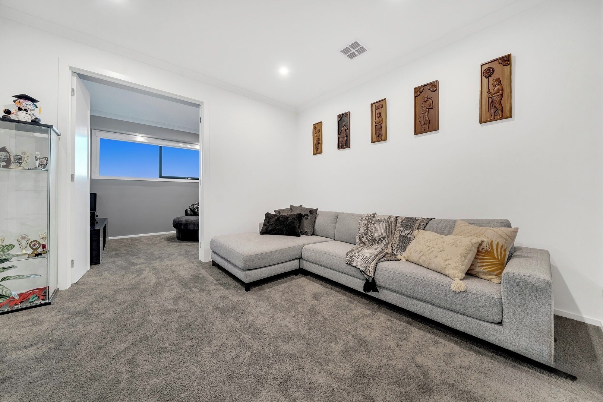 A modern living room with a grey sectional sofa, a glass cabinet with decorative items, and a series of wooden wall art pieces.