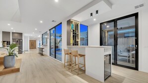 A modern kitchen with a built-in fridge, a dining area with bar stools, and a large sliding glass door leading to a balcony. - Luxe designer house with Pool, Cinema & Gym (Clyde North)