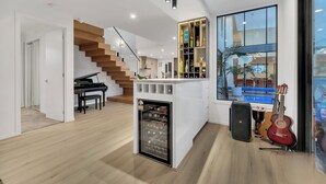 A modern living room with a piano, a wine rack, and a large window with a view of a pool. - Luxe designer house with Pool, Cinema & Gym (Clyde North)