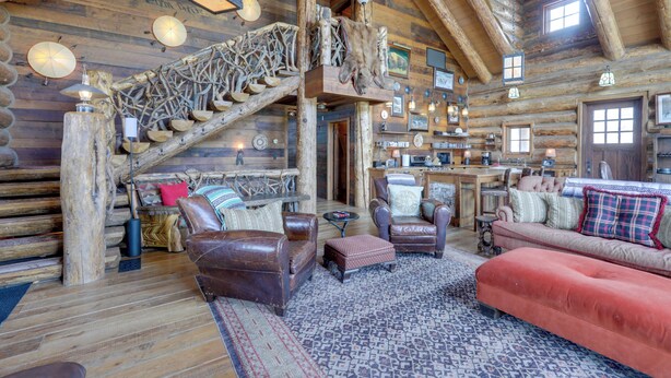 A log cabin interior with a wooden staircase, leather furniture, and a cozy fireplace.