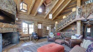 A log cabin interior with a fireplace, leather furniture, and a wooden staircase.