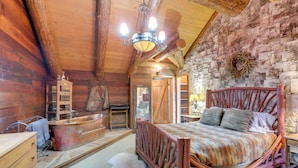 A rustic wooden room with a large bed, a wooden dresser, a bathtub, and a stone wall.