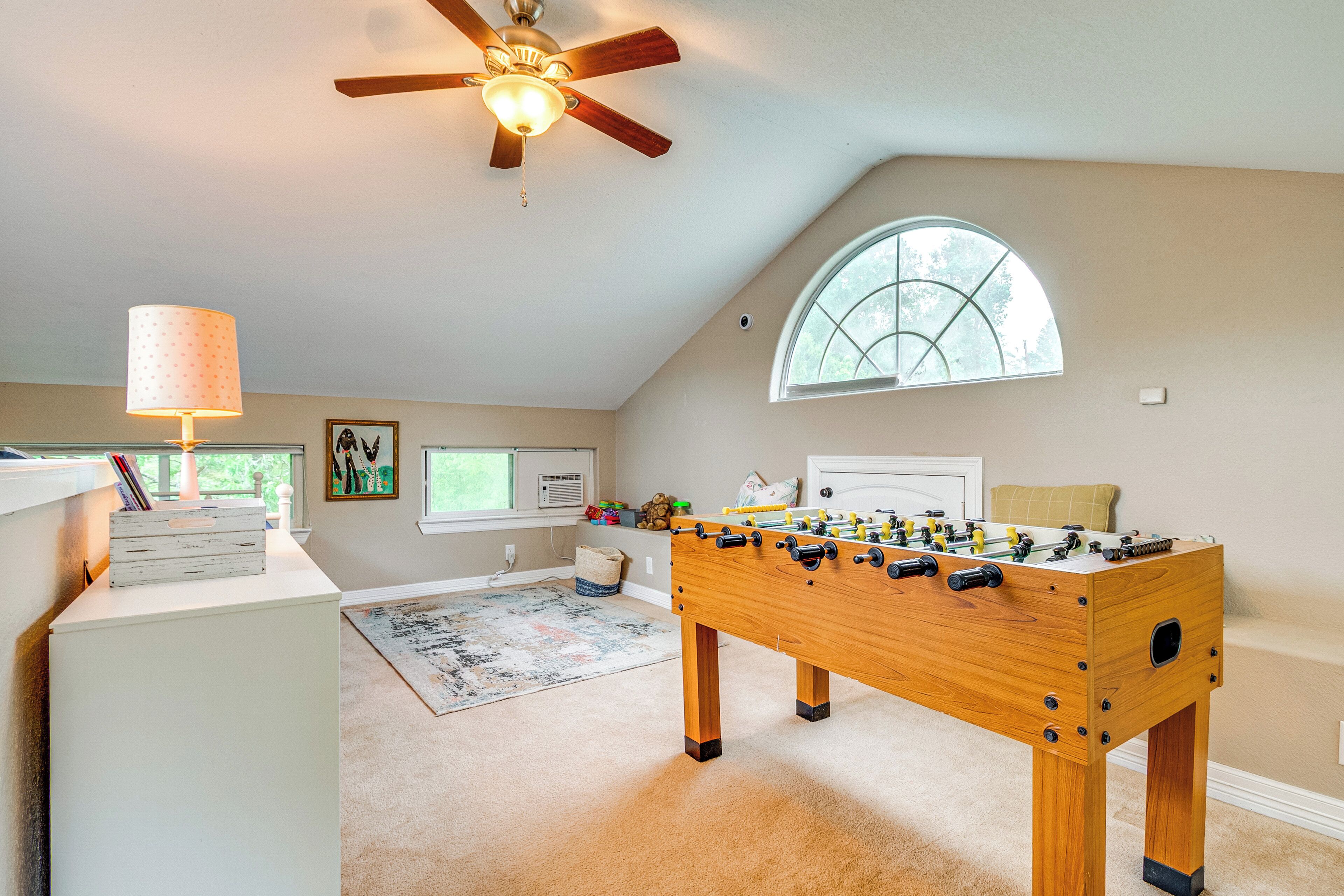 A cozy room with a foosball table, a ceiling fan, a window with a view, and a lamp.