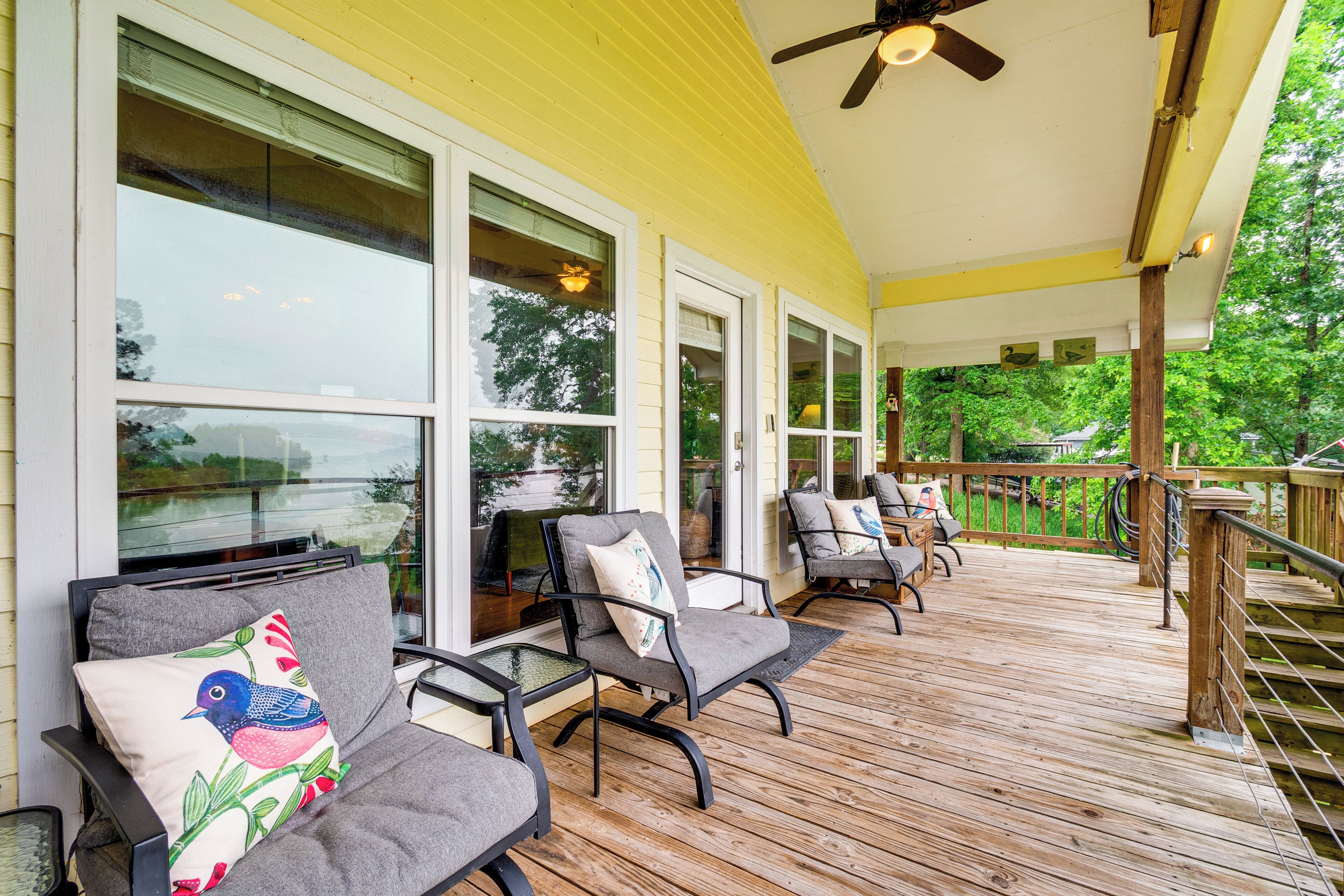 A covered deck with outdoor furniture, large windows, and a ceiling fan.