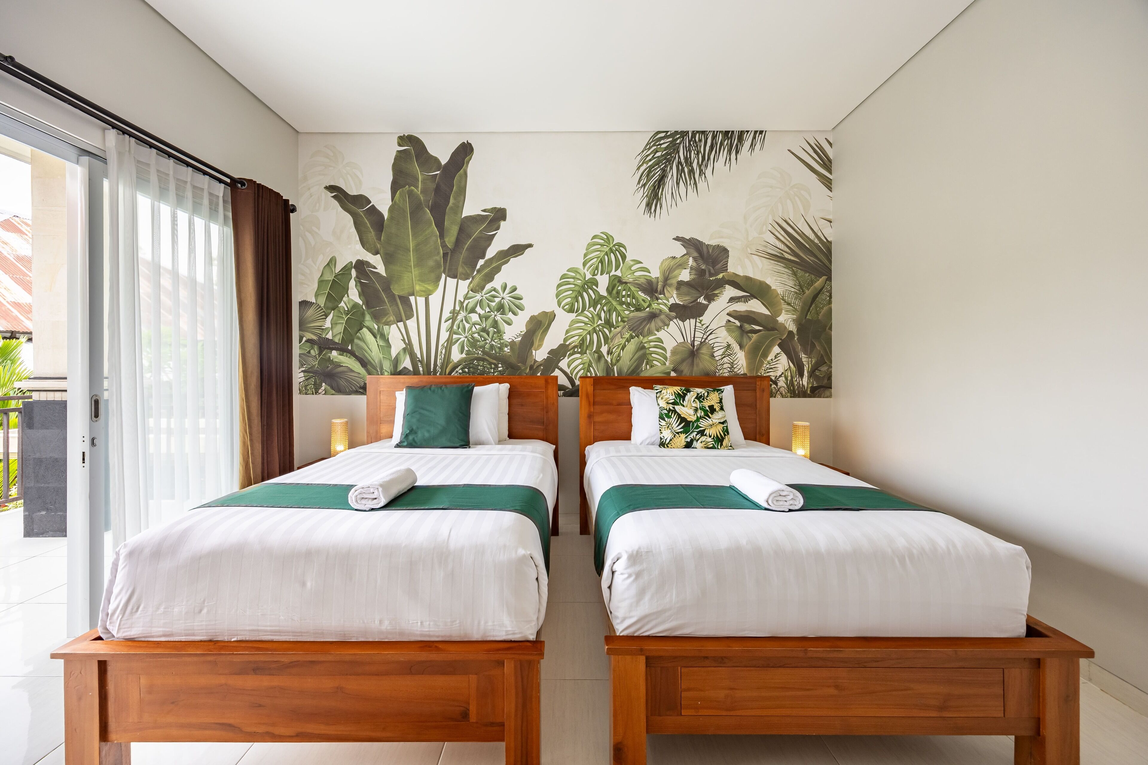 Una habitación de hotel con dos camas de madera, ropa de cama blanca y un mural tropical en la pared.