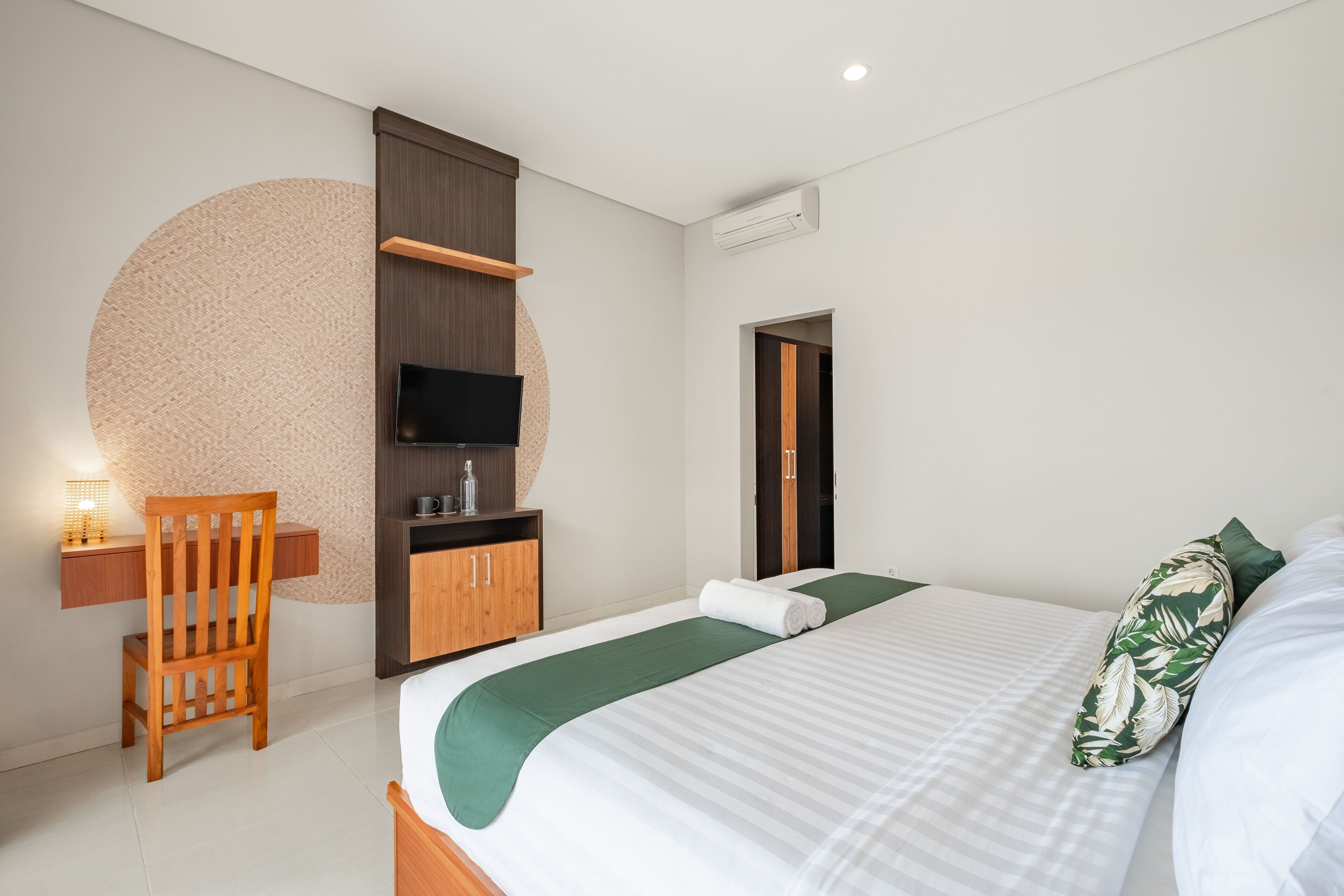 Una habitación de hotel moderna con una cama, una silla de madera, un escritorio con lámpara, un televisor y un armario.