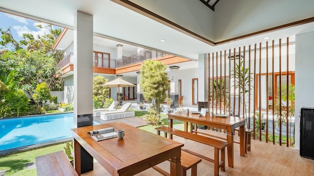 Amplio espacio interior con piscina, muebles de madera y un balcón con vistas a la vegetación.