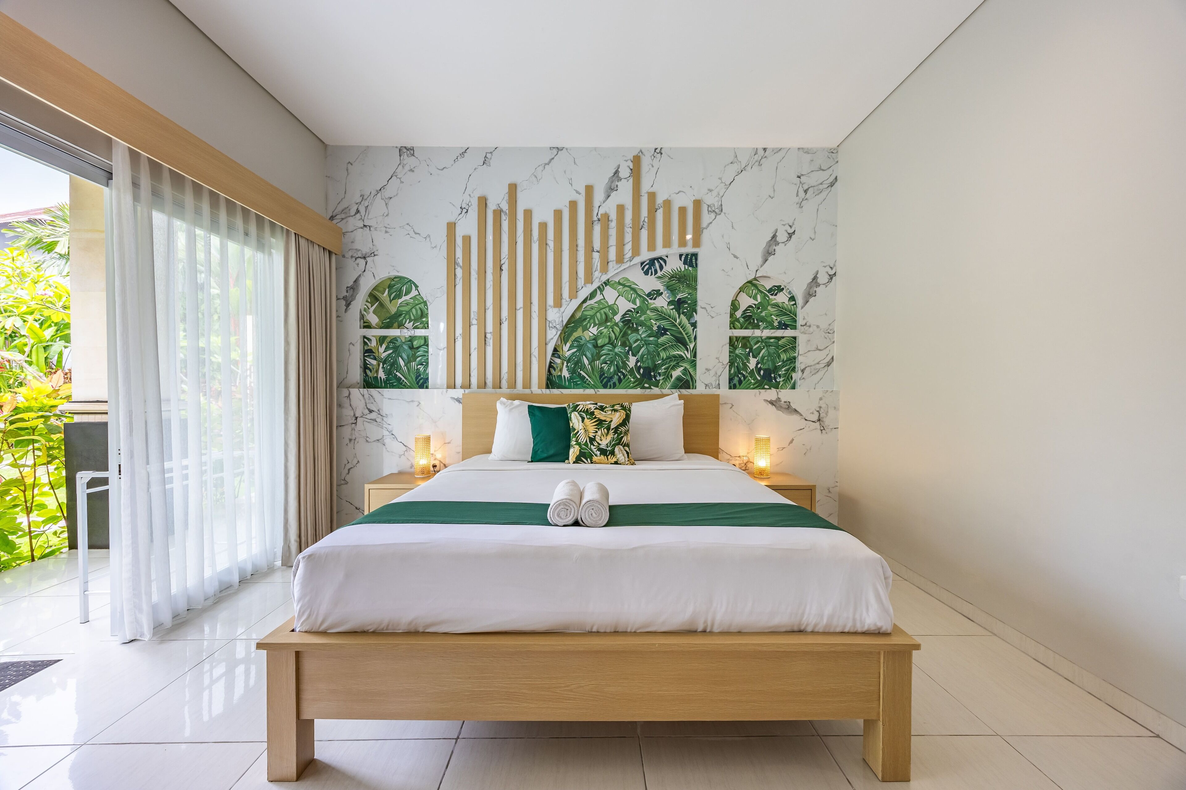A modern hotel room with a large bed, a marble-patterned wall, and a view of greenery.