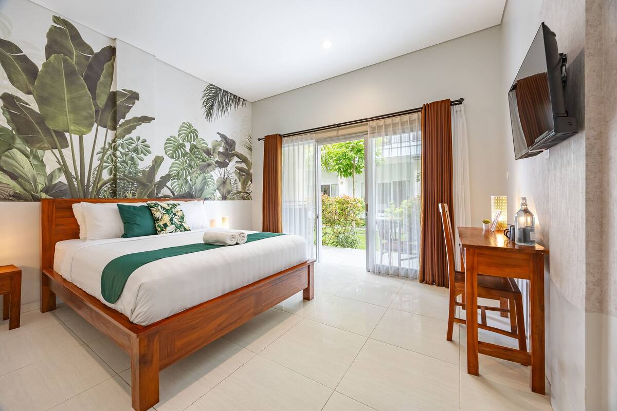 A bedroom with a wooden bed, a desk, a TV, and a large window with curtains.