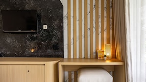 Una habitación moderna con un escritorio de madera, un televisor instalado en una pared de mármol y una mesita con una lámpara y una planta.