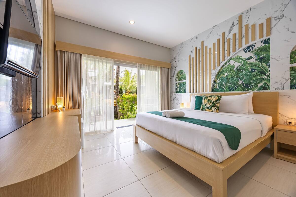 A modern hotel room with a large bed, a wooden desk, a marble wall mural, and a view of greenery outside.