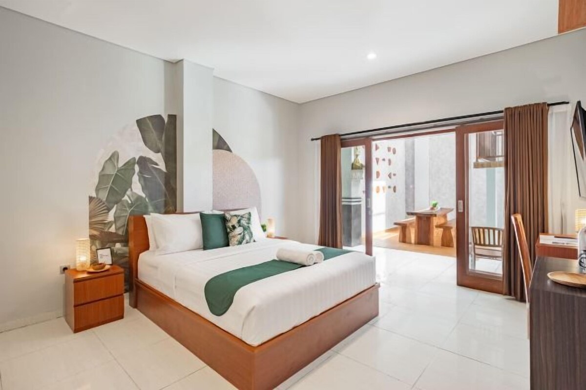 A modern bedroom with a large bed, a nightstand, a desk, and a view of the outdoor area.