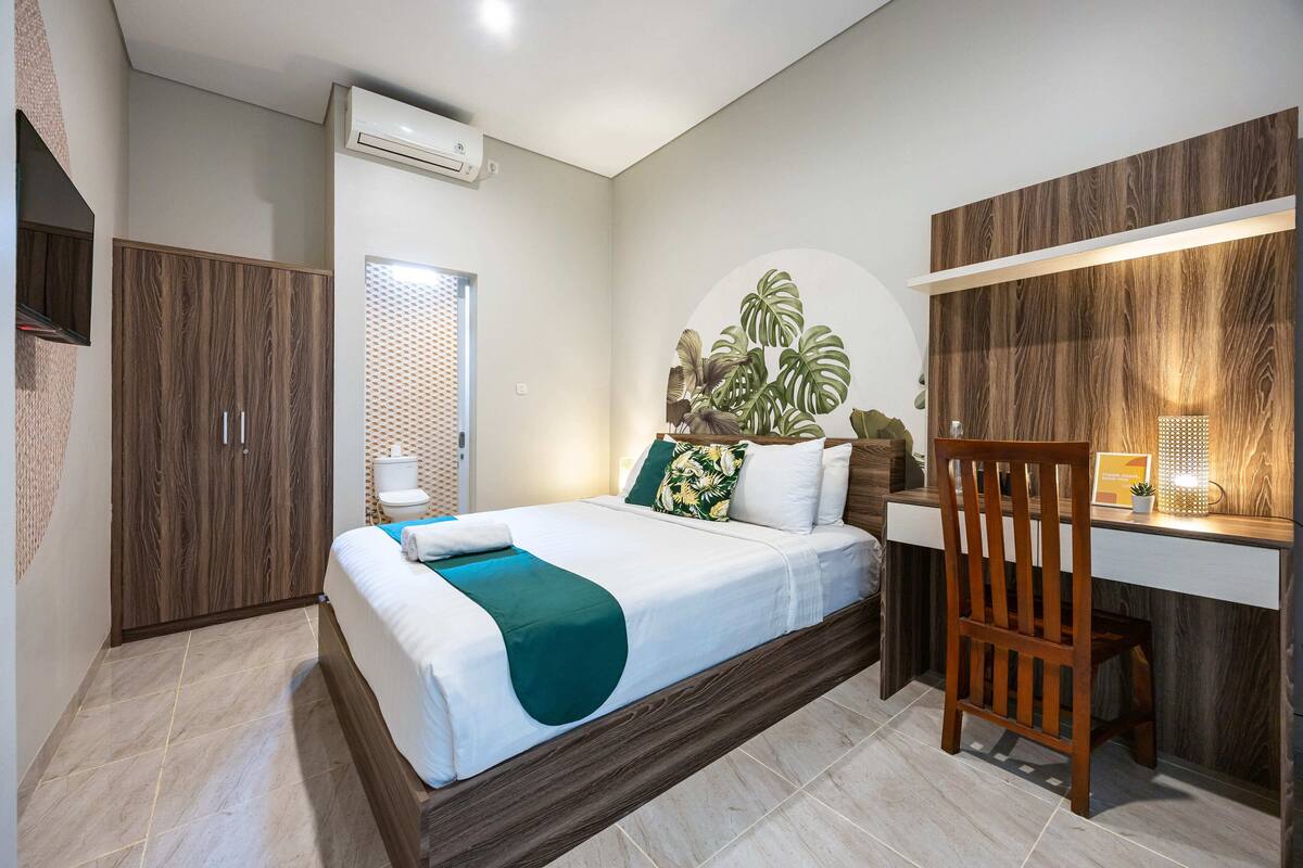 A bedroom with a bed, a desk, a chair, a wardrobe, and a plant.