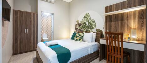 A bedroom with a bed, a desk, a chair, a wardrobe, and a plant.