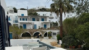 Een terras met witte meubels, een stenen vloer en uitzicht op witte gebouwen met blauwe deuren.