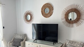 Een kamer met een televisie, rieten meubels en decoratieve spiegels.