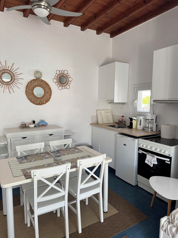 Una cocina compacta con armarios blancos, un refrigerador pequeño, una cafetera y un ventanal.