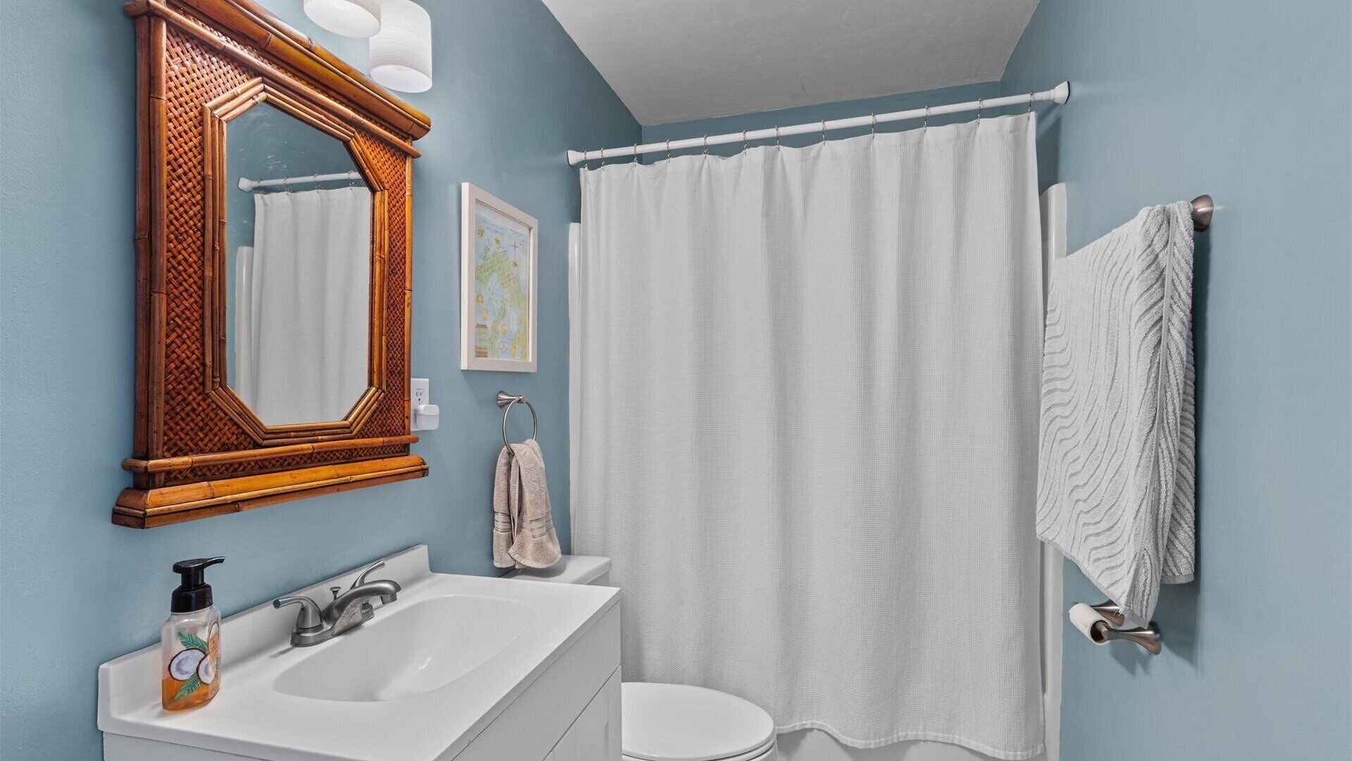 Un baño con un espejo de marco de madera, un lavamanos blanco, un inodoro y una cortina de ducha.