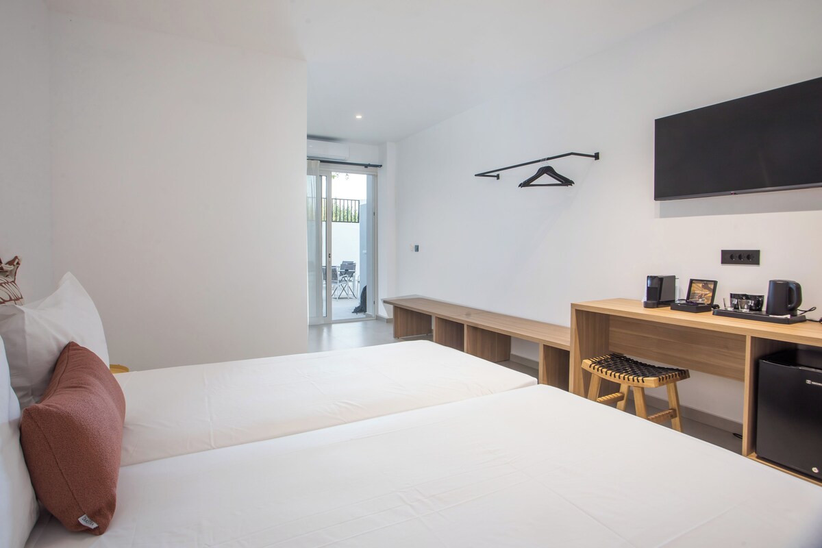 A modern hotel room with two beds, a wooden desk, a black refrigerator, and a TV mounted on the wall.